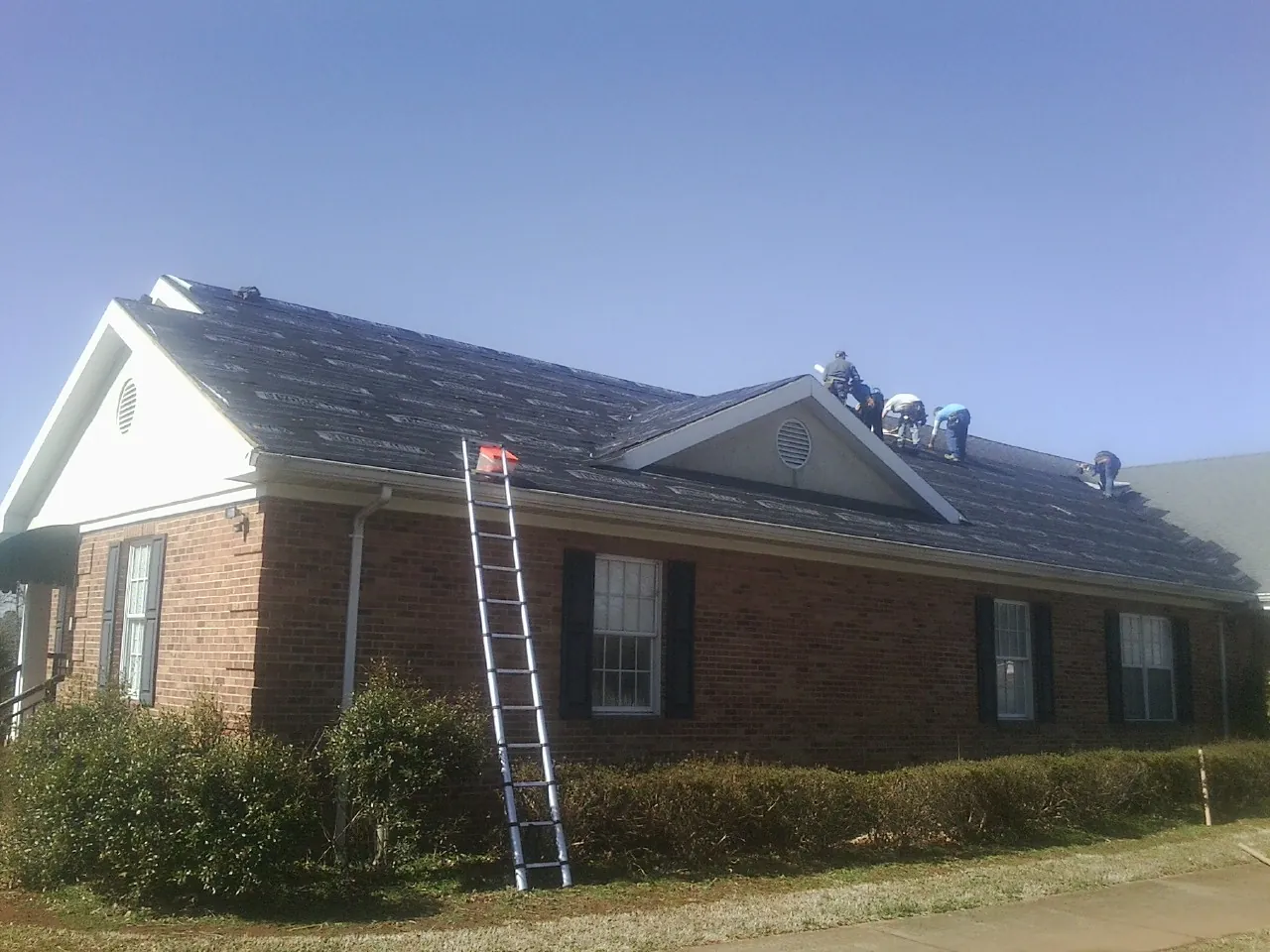Crew tearing shingles off a brick ranch roof with a ladder set — Emergency Roof Repair work by our crew in Davis